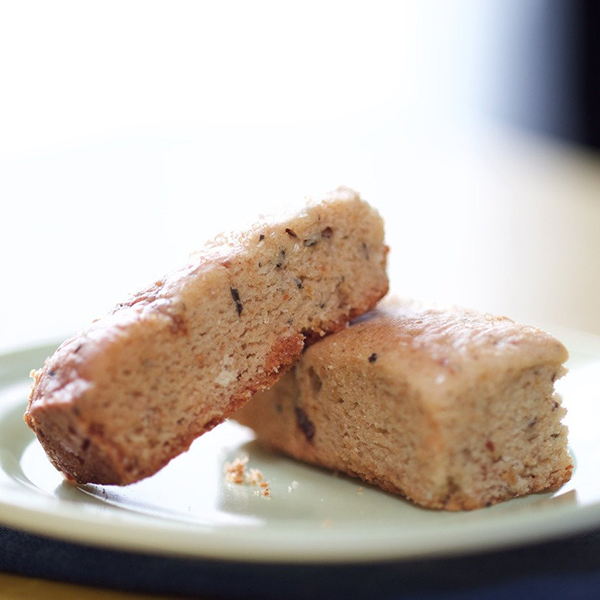 Two gluten-free spiced fig Subarz stacked on a light green plate, showcasing their golden-brown exterior and soft, crumbly texture. The bars are speckled with aromatic herbs and fig pieces, highlighting their unique blend of flavors. The close-up shot captures their rich, artisanal appearance with a blurred background for a warm, inviting feel.